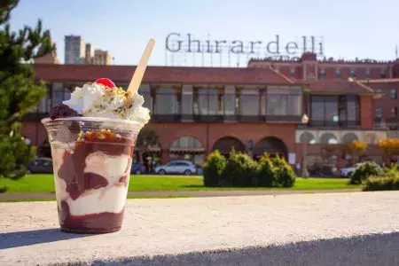 A chocolate sundae sits in the foreground with Ghirardelli Square in the background.