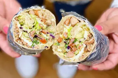 Um burrito estilo mission , app em papel alumínio e cortado ao meio, é mostrado para a câmera.