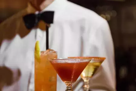 A server wearing a bowtie presents a tray of cocktails at Absinthe Restaurant in San Francisco.