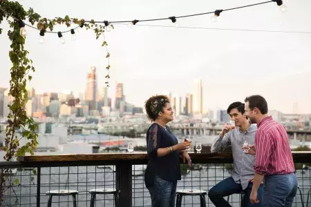 Three people gather around an outdoor table on the roof deck of Anchor Distilling in San Francisco, California.