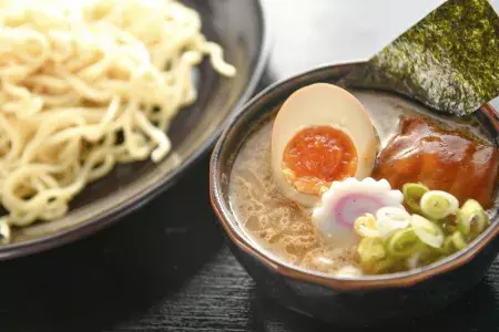 Close up shot of a bowl of noodles and a bowl of ramen soup with a poached egg, sliced in half.