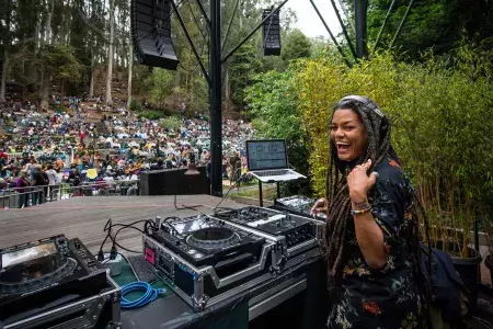 A woman DJing at the Stern Grove Festival looks over her shoulder and smiles into the camera.