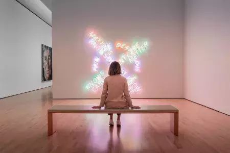 A woman, seated on a bench, looks at a piece of contemporary light art at SF MOMA in San Francisco.