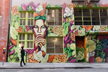 A woman looks up at a brightly colored mural on the side of a brick building in San Francisco.