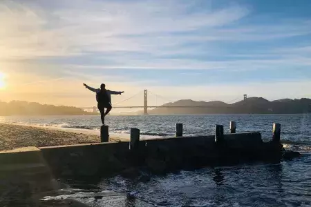 Uma mulher está em um píer no bairro Marina de São Francisco, olhando para a Golden Gate Bridge .