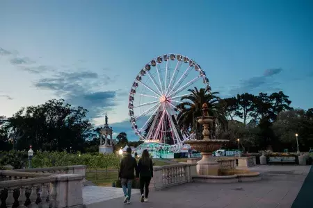 A couple walks toward the SkyStar Ferris Wheel at dusk.