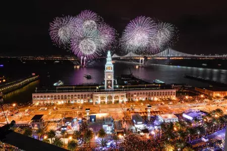 Fireworks explode over top of the Ferry Building, with the Bay Bridge in the background. San Francisco, California.