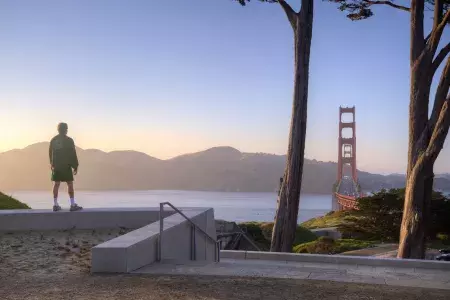 A man overlooks the Golden Gate Bridge with mountains in the background.