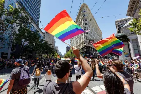 People walking in the San Francisco Pride parade wave rainbow flags.