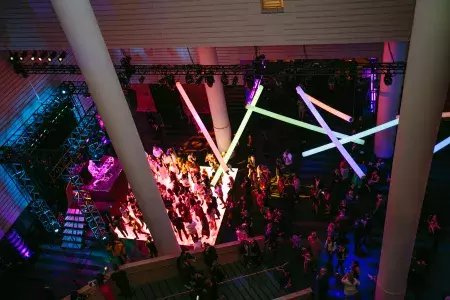 Image of people on a dance floor lit by rainbow neon lights hanging from ceiling