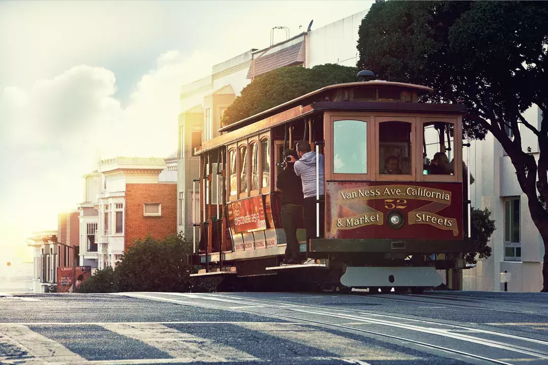 A cable car rounds a hill in San Francisco with passengers looking out the window.