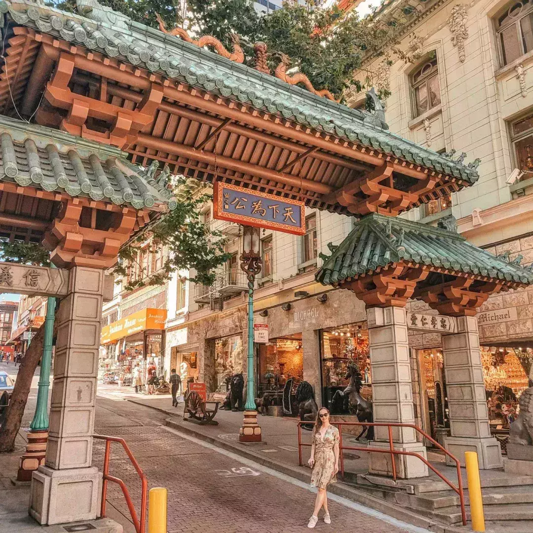 A woman poses in front of an ornate gate marking the entrance of San Francisco's Chinatown.