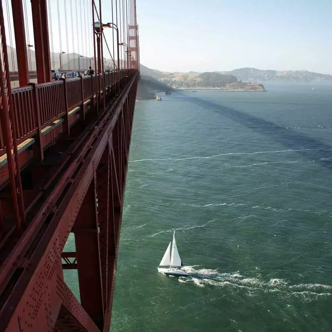 A small sailboat passes beneath the Golden Gate Bridge in the San Francisco Bay.