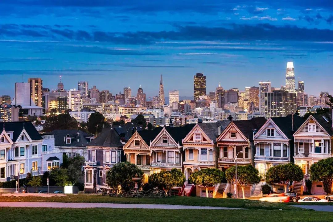 As famosas Painted Ladies da Alamo Square são retratadas tendo como pano de fundo o horizonte de São Francisco ao entardecer.