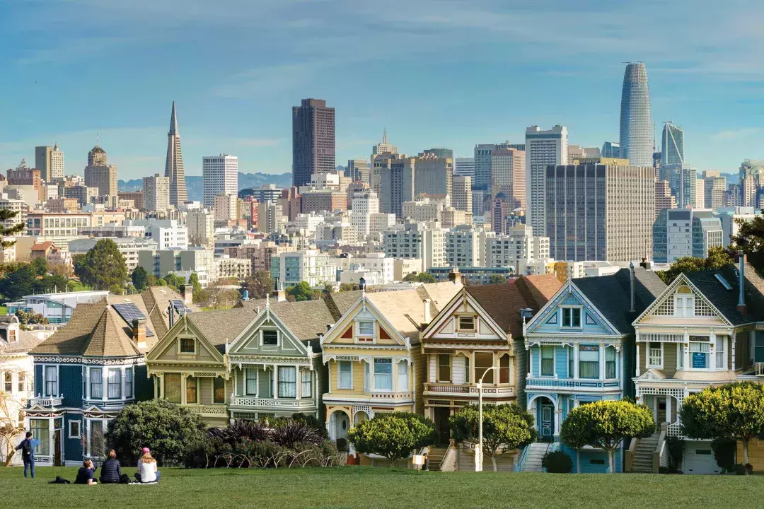 Os piqueniques sentam-se na grama do Alamo Square Park com as Painted Ladies e o horizonte de São Francisco ao fundo.