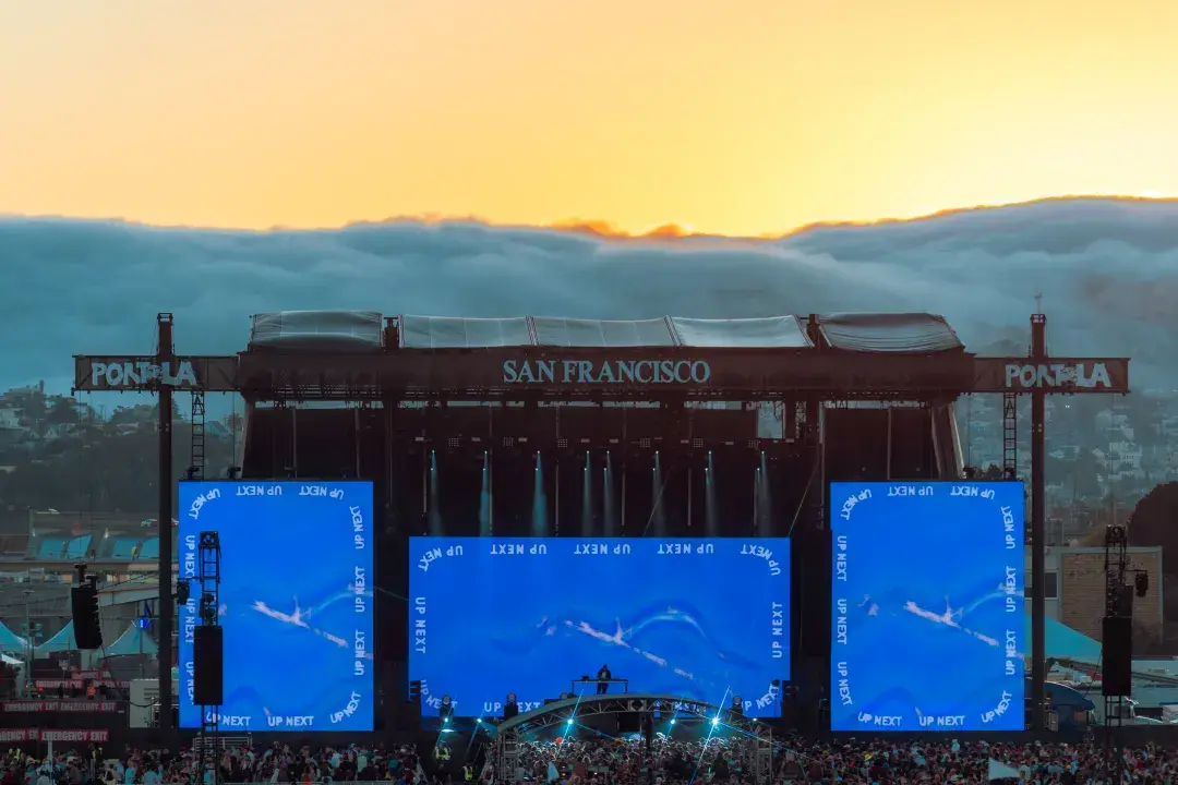 Fog spilling down San Francisco hills behind stage for music festival at sunset.