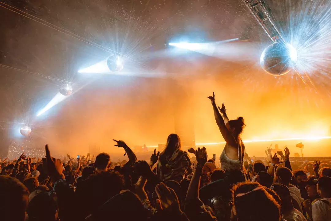men and women dancing under yellow lights and disco balls at music festival