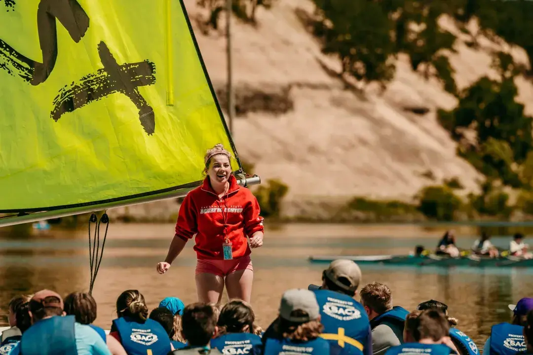 Woman stands in front of crowd and instructs them in boating on reservoir
