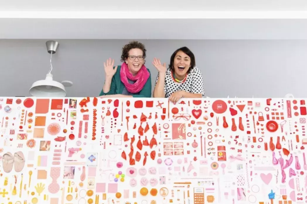 Women standing waving from indoor balcony with colorful art