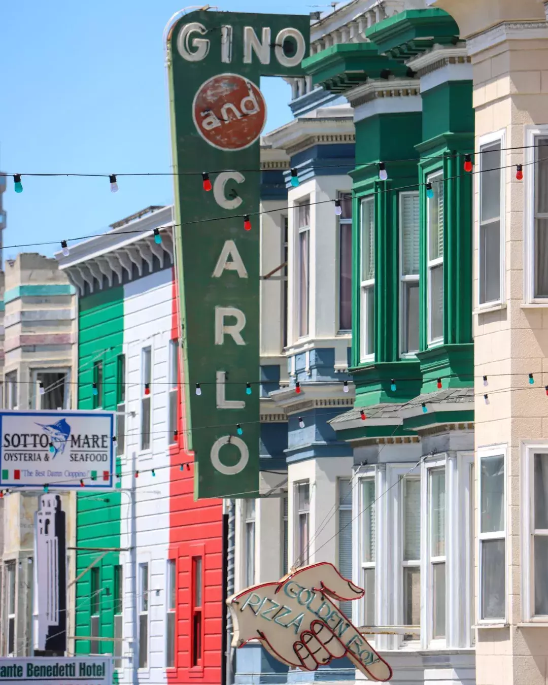 Large sign reading "Gino and Carlos" with Italian flag colored building in background 