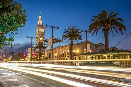 the ferry building at illuminated at dusk with car headlights passing in front