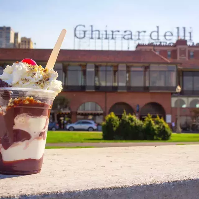 A chocolate sundae sits in the foreground with Ghirardelli Square in the background.