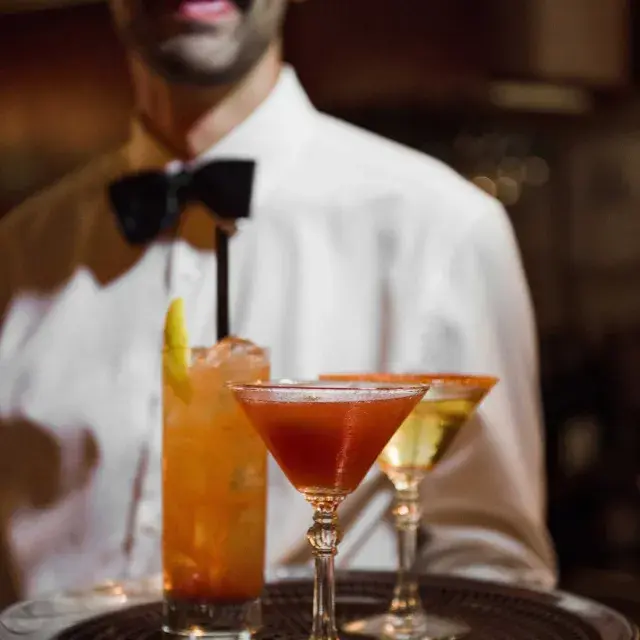 A server wearing a bowtie presents a tray of cocktails at Absinthe Restaurant in San Francisco.
