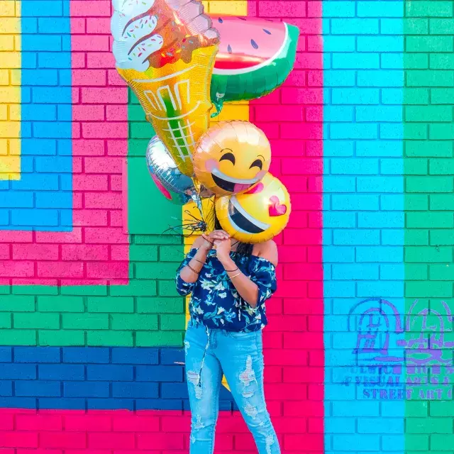 Uma menina comemora seu aniversário com balões em frente a um mural colorido.