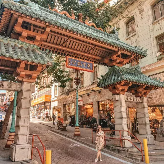 Uma mulher posa em frente a um portão ornamentado que marca a entrada da Chinatown de São Francisco.