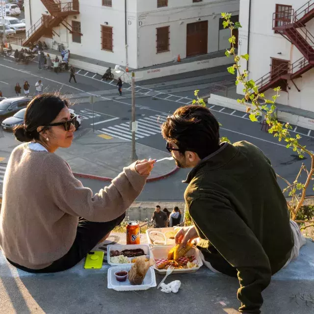 Um casal janta ao ar livre no Fort Mason Center, em São Francisco. A mulher alimenta seu companheiro com um gostinho de comida.