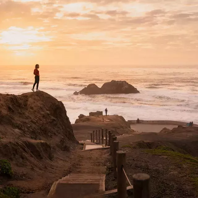 Duas pessoas estão sobre rochas com vista para o oceano em Sutro Baths, em São Francisco.