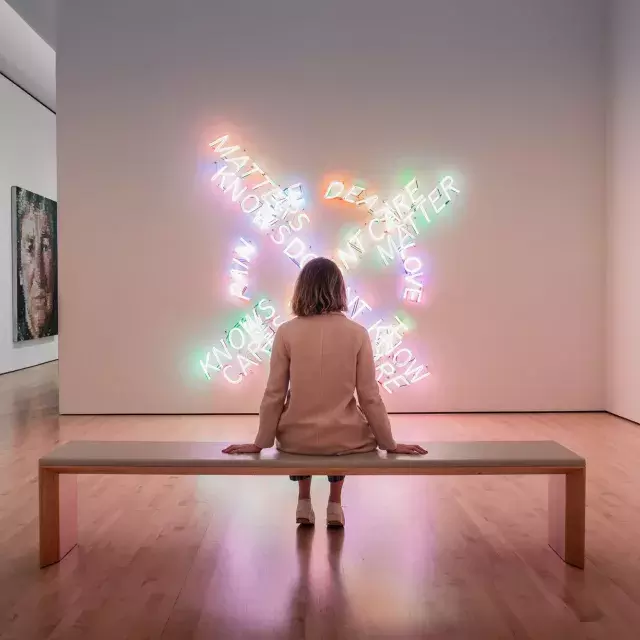 A woman, seated on a bench, looks at a piece of contemporary light art at SF MOMA in San Francisco.