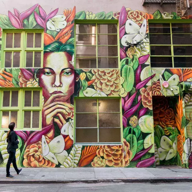 A woman looks up at a brightly colored mural on the side of an ornate building in San Francisco.