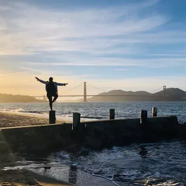 A woman stands on a pier in San Francisco's Marina neighborhood, looking out at the Golden Gate Bridge.