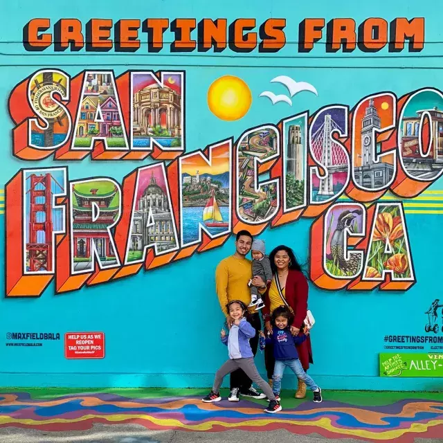 A family posing for a photo in front of a San Francisco mural