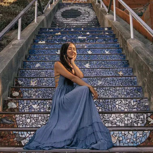 A woman poses sitting on the 16th Avenue tiled stairs in the Sunset neighborhood of San Francisco.