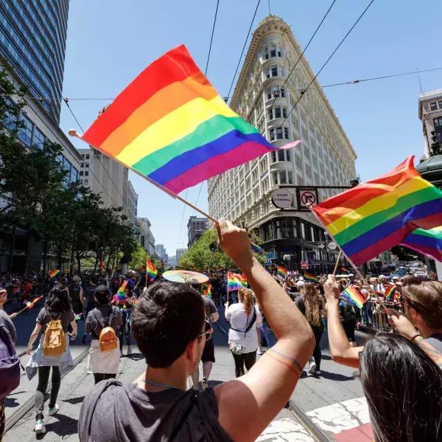 People walking in the San Francisco Pride parade wave rainbow flags.