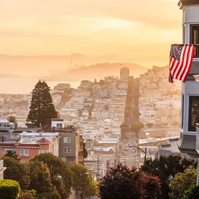 丘の頂上から見たサンフランシスコの眺め。前景にはアメリカ国旗がはためいています。