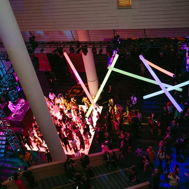 Image of people on a dance floor lit by rainbow neon lights hanging from ceiling