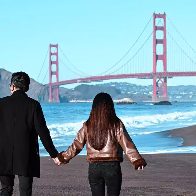 Couple holding hands at Baker Beach with Golden Gate bridge in background 