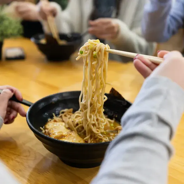 Person lifting ramen noodles out of a bowl with chopsticks