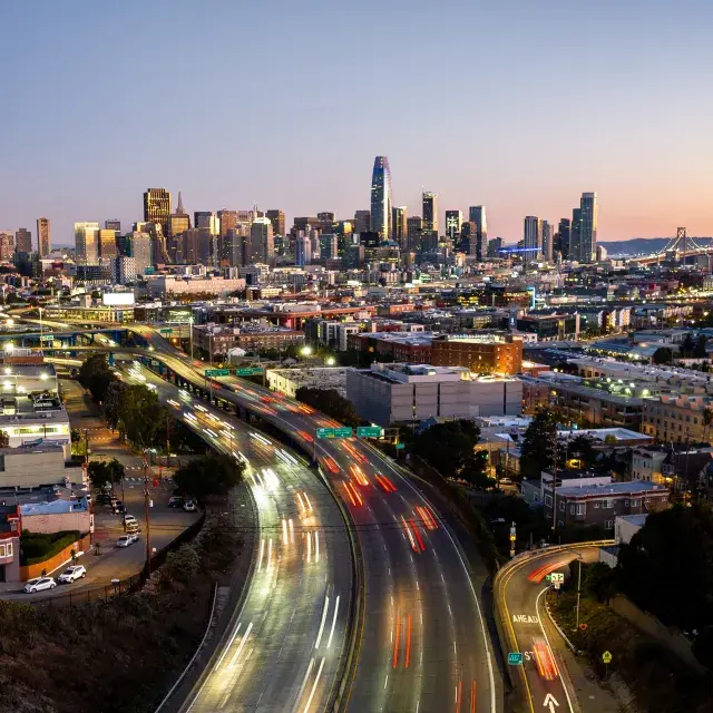 Downtown San Francisco skyline at dusk, with cars rushing on freeway heading in and out of the city.