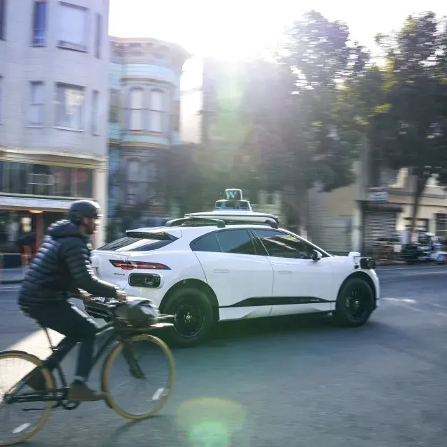 Person riding a bicycle behind a Waymo car