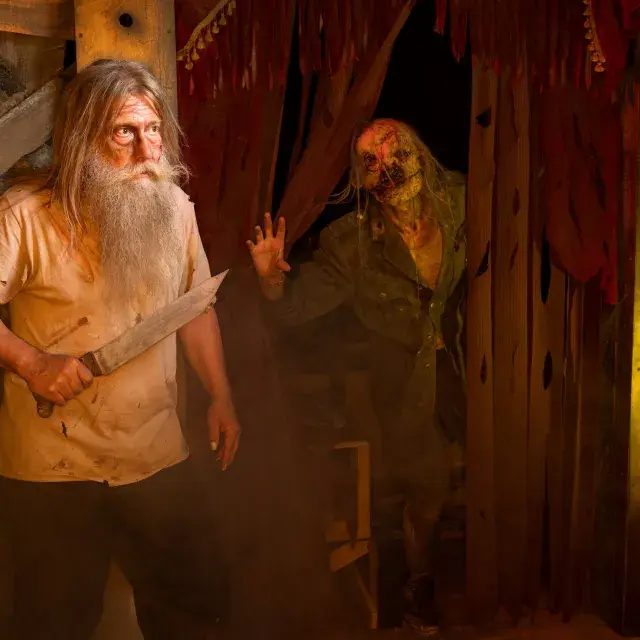 Man with long gray beard holding knife with a ghoulish monster behind him 