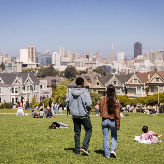 Two people walking in front of the painted ladies in Alamo Square Park