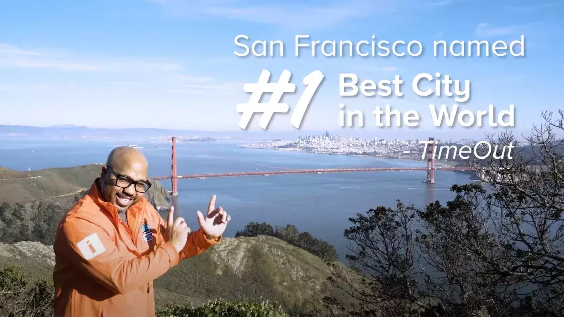 A man poses in front of the Golden Gate Bridge with onscreen text that reads "San Francisco Voted #1 City in the World - TimeOut""
